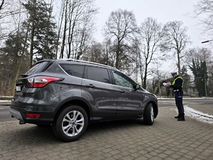 Zdjęcie przedstawia umundurowanego policjanta oraz samochód osobowy.