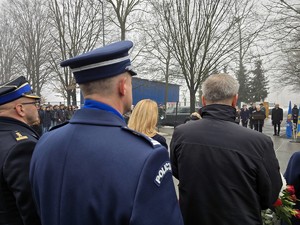 Zdjęcie przedstawia umundurowanego policjanta oraz uczestników uroczystości.