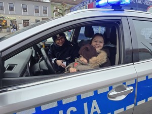 Zdjęcie przedstawia umundurowaną policjantkę oraz uczestników wydarzenia w radiowozie.