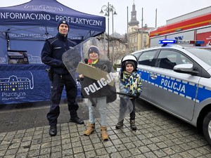 Zdjęcie przedstawia uczestników wydarzenia, umundurowanego policjanta oraz radiowóz.