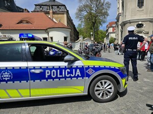 Zdjęcie przedstawia umundurowanego policjanta obok radiowozu.
