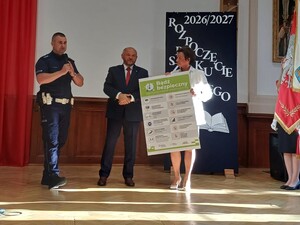 Zdjęcie przestawia policjanta wraz z innym mężczyzną i kobietą podczas uroczystości rozpoczęcia roku szkolnego.