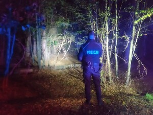 Zdjęcie przedstawia policjanta w lesie podczas nocnych poszukiwań.