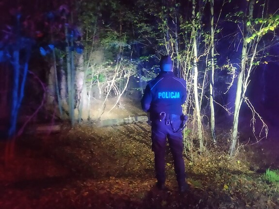 Zdjęcie przedstawia policjanta w lesie podczas nocnych poszukiwań.